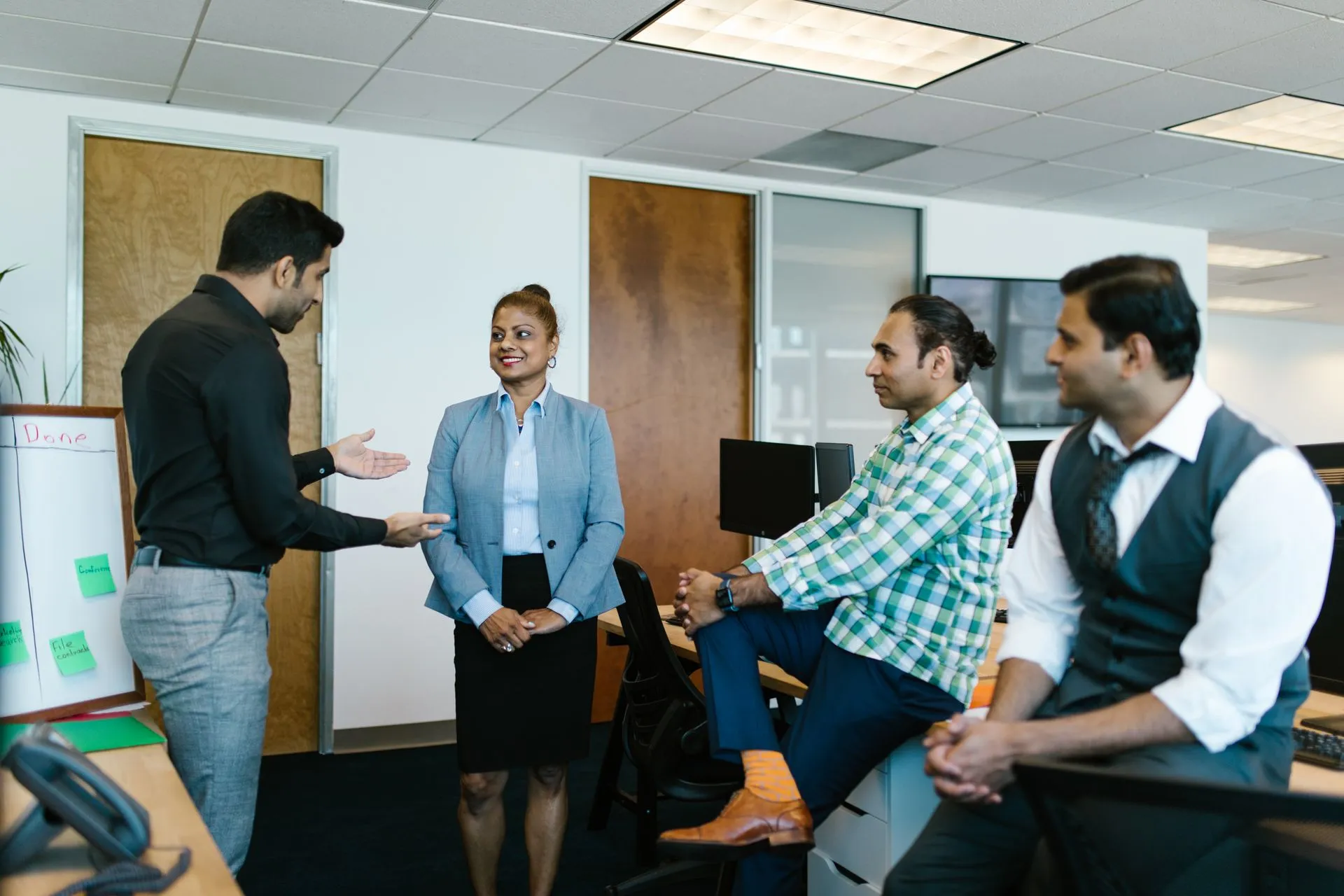South Asian team discussing project progress beside a task board in a bright office